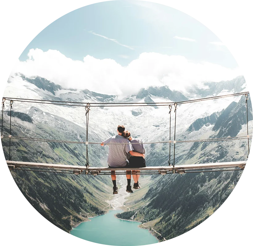 a couple sitting on a suspended bridge overlooking a river and valley
