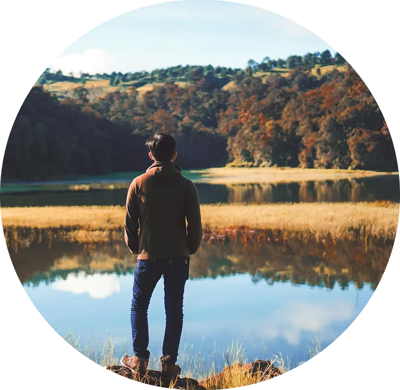 man standing on rock looking out at lake and fields